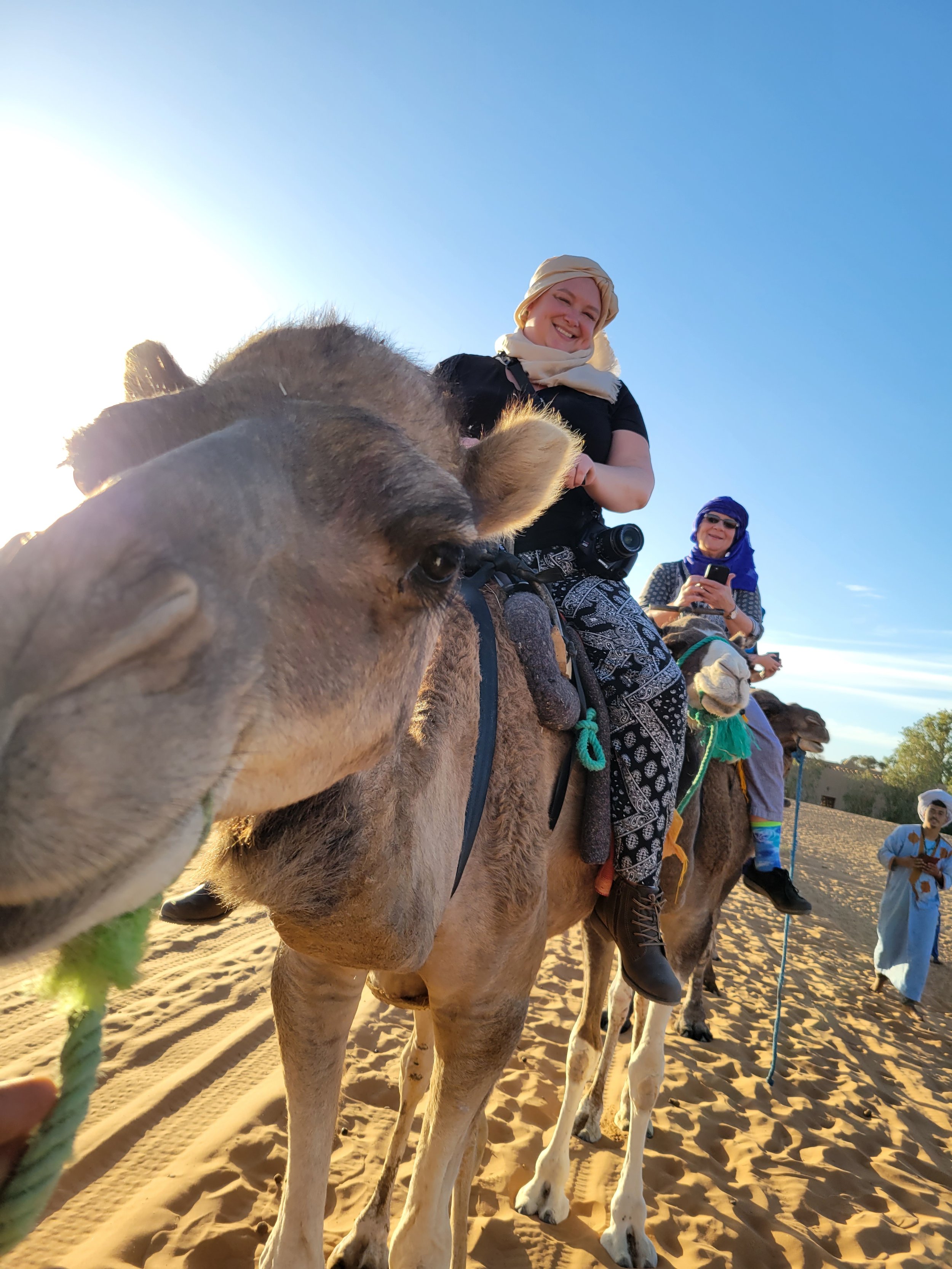 Two women with turbans ride camels through the Sahara desert