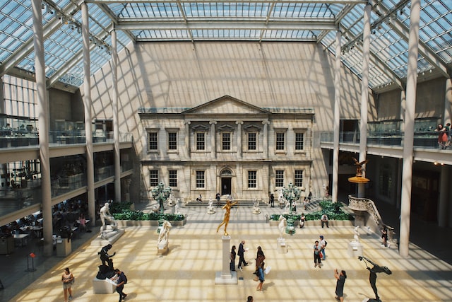 Interior shot of an atrium. Sculptures are scattered throughout and there is a stone building facade at one end