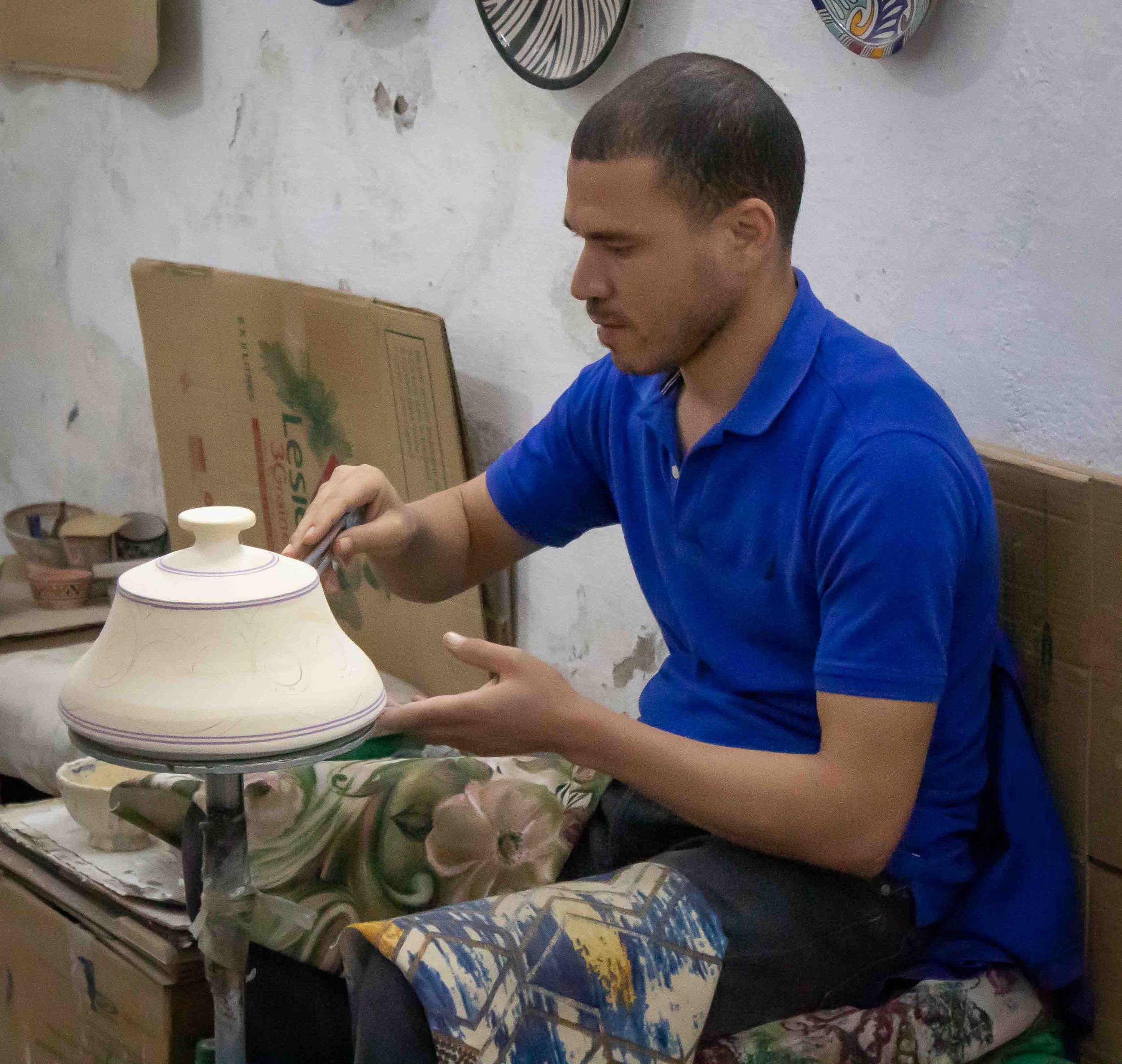 A man sits while he paints a piece of pottery