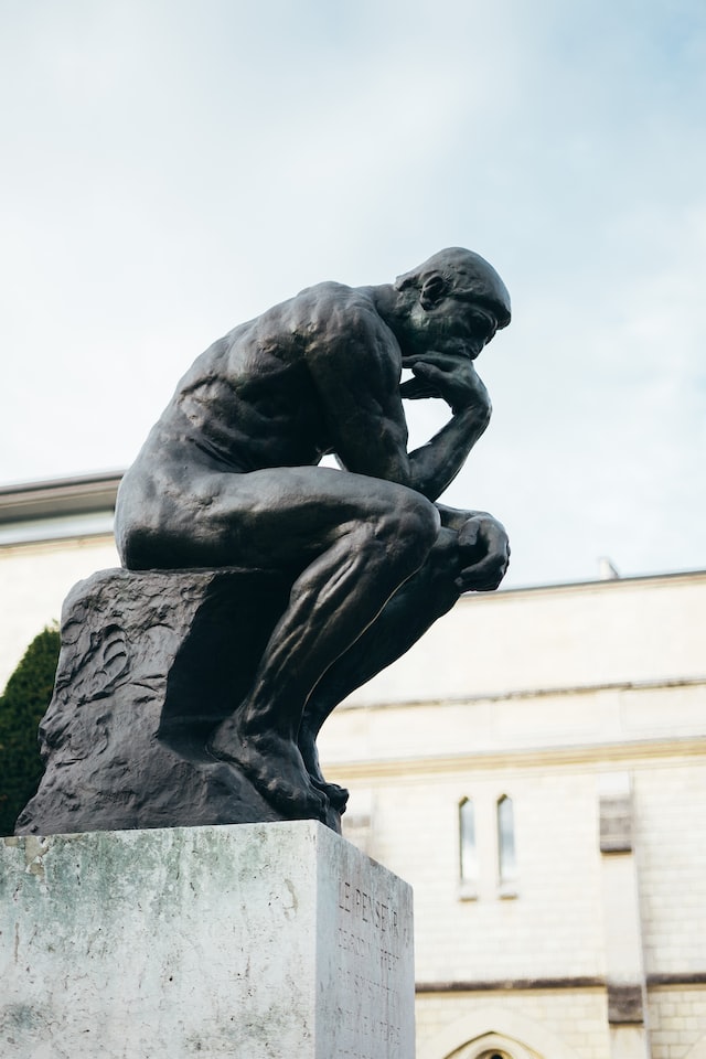 A statue of a man sitting, his head on his hand in a state of thought