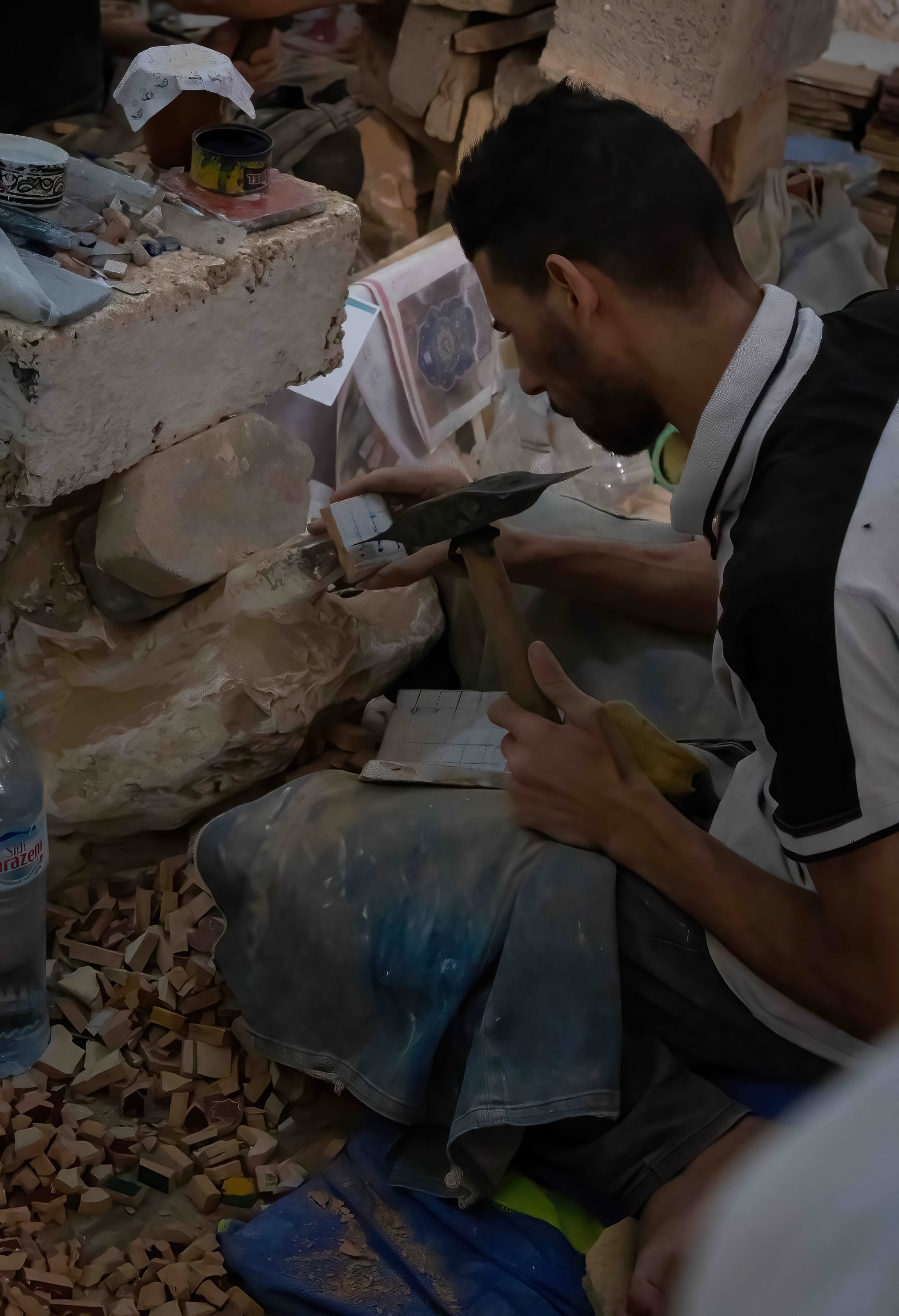 A tile worker sits and breaks pieces of tile apart to create mosaic pieces.