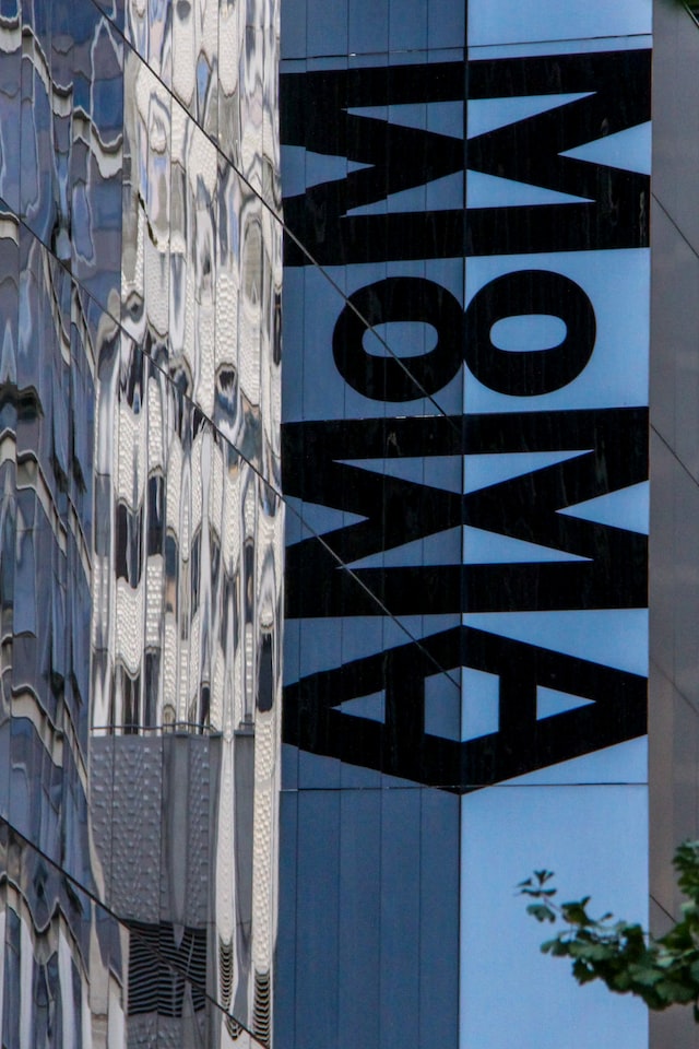 Large sign spelling MoMA hanging vertically from a silver city building